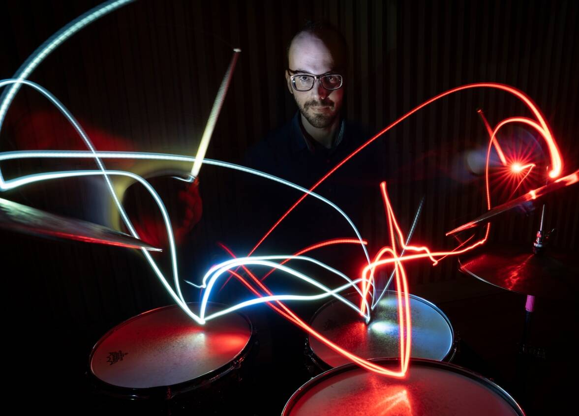 Márton Juhász sitzt im Dunkeln hinter einer Drumsbatterie spielt mit professioneller Leichtigkeit seine Rhythmen, welche als Lichtspuren seiner Werkzeuge gekonnt visuell dargestellt sind.